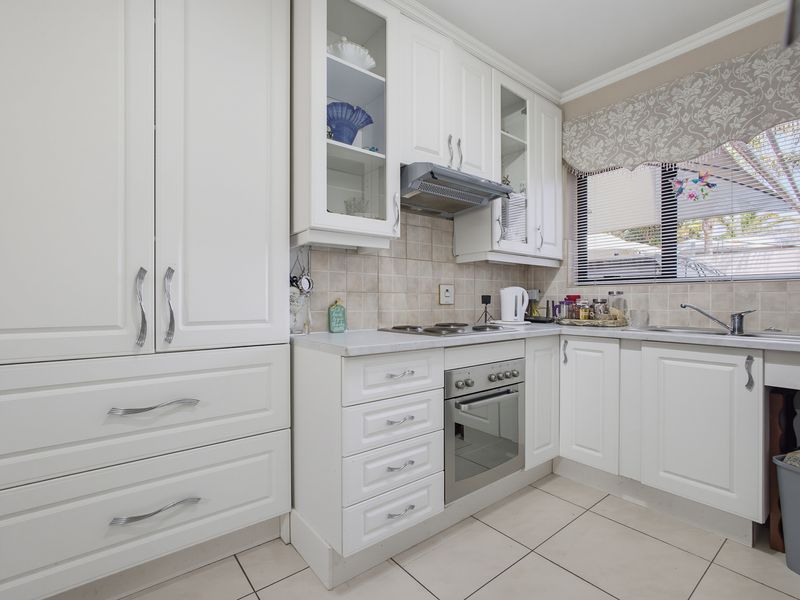 A well-maintained kitchen featuring white cabinetry, built-in oven and hob, tiled backsplash, and neutral floor tiles, offering a clean and functional workspace.