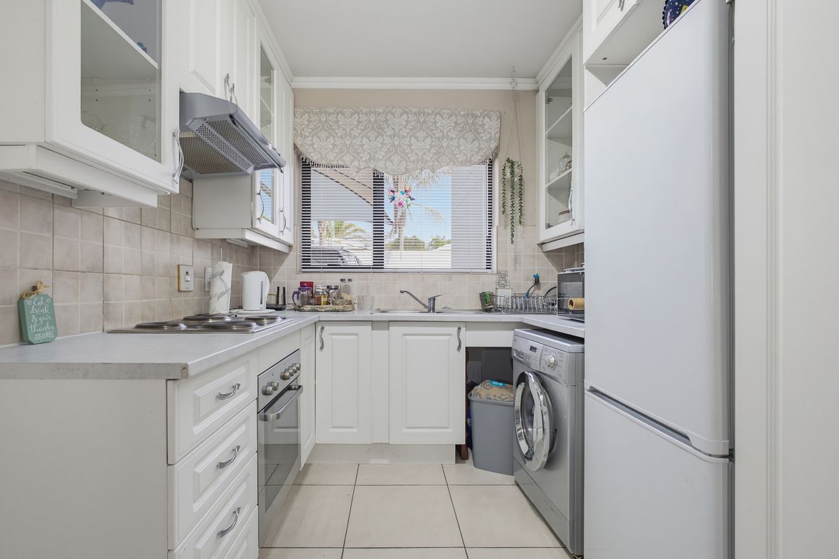 A compact, well-maintained kitchen featuring white cabinetry, tiled backsplash, built-in oven, electric hob, and integrated laundry appliance space.