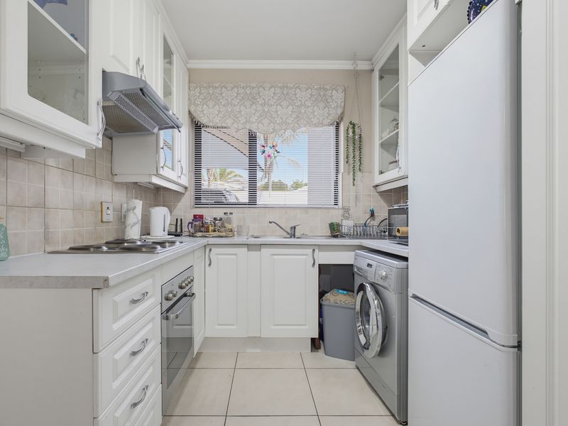 A compact, well-maintained kitchen featuring white cabinetry, tiled backsplash, built-in oven, electric hob, and integrated laundry appliance space.