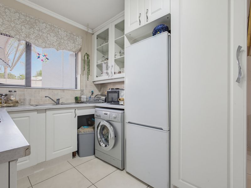 A functional laundry area featuring built-in white cabinetry, a stainless steel sink, tiled backsplash, and dedicated space for appliances.
