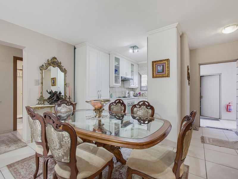 Open plan dining area adjacent to a functional kitchen with white cabinetry, featuring tiled flooring and neutral wall finishes throughout.