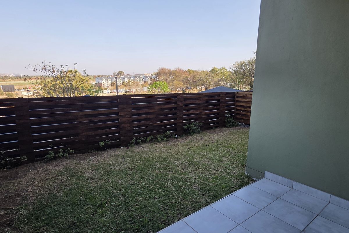 A private rear garden featuring a tiled patio area and timber slat fencing, offering an open outlook over the surrounding estate.
