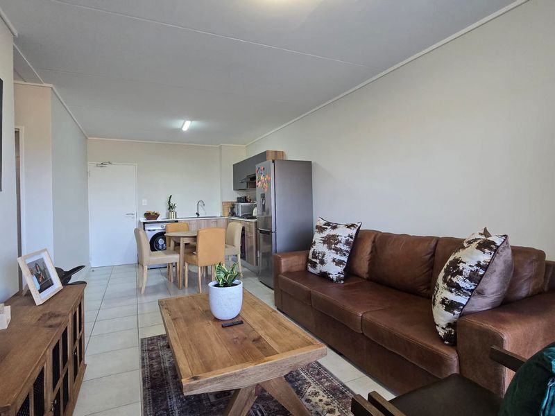 An open-plan living and kitchen area featuring tiled flooring, functional cabinetry, and a compact laundry connection point.