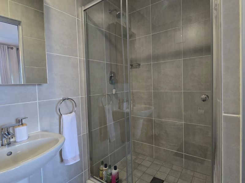 Modern bathroom featuring a glass-enclosed shower with tiled walls, a pedestal washbasin, and contemporary chrome fixtures.