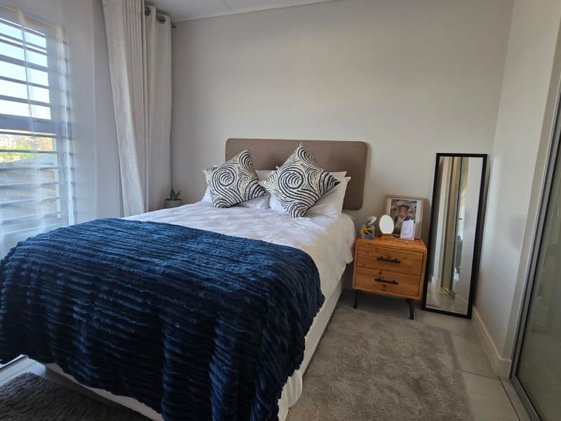 A well-maintained bedroom featuring tiled flooring, a built-in wardrobe, and large windows with fitted blinds, offering a bright and comfortable living space.