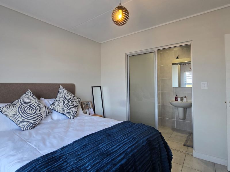 A well-maintained bedroom featuring tiled flooring, a modern pendant light, and an en-suite bathroom accessed via a sliding door.