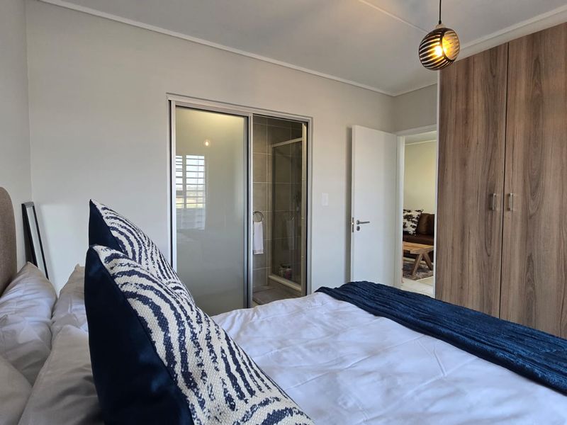 A well-maintained bedroom featuring built-in wooden wardrobes, neutral finishes, and direct access to an en-suite bathroom.