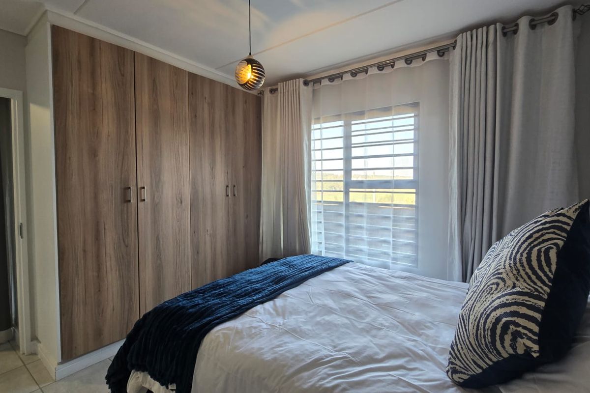 A well-maintained bedroom featuring floor-to-ceiling wood-finish built-in cupboards, a window with security bars, and modern pendant lighting.