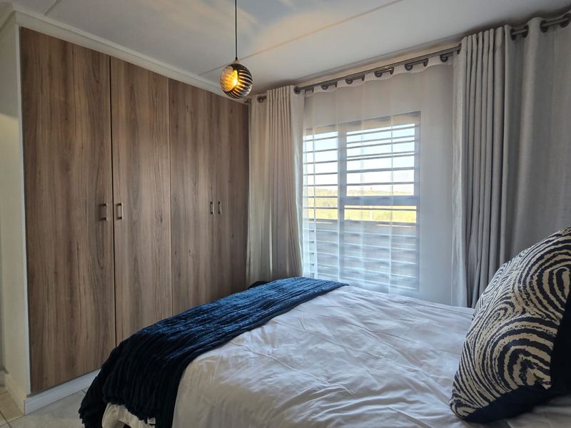 A well-maintained bedroom featuring floor-to-ceiling wood-finish built-in cupboards, a window with security bars, and modern pendant lighting.