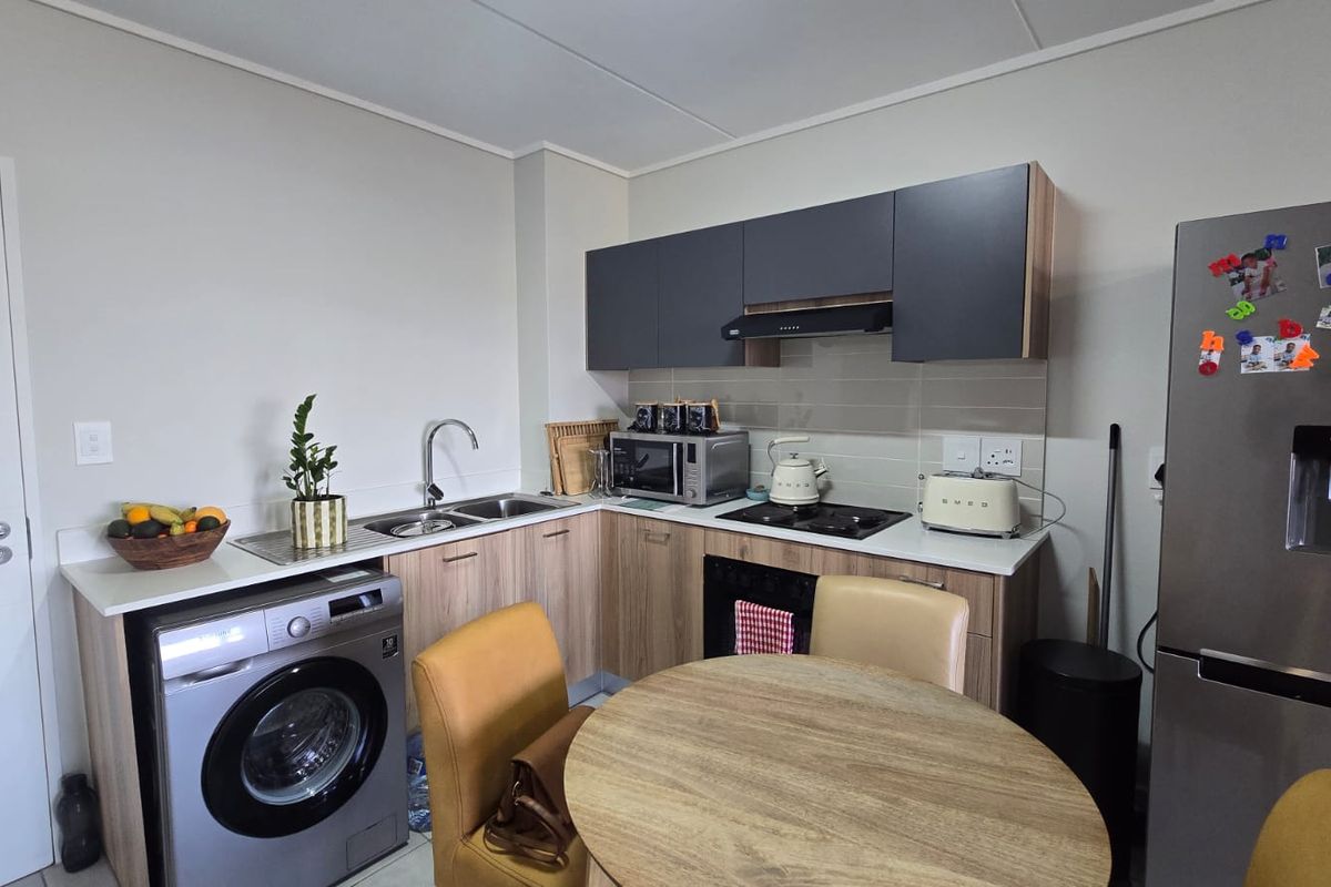 Modern kitchen featuring wood-finish cabinetry, light countertops, integrated appliances, and a tiled backsplash, offering a functional and contemporary cooking space.