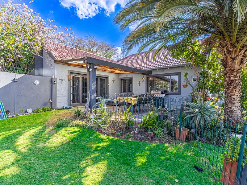A well-maintained rear exterior view featuring a covered patio with a timber pergola, sliding glass doors, and a landscaped garden area.