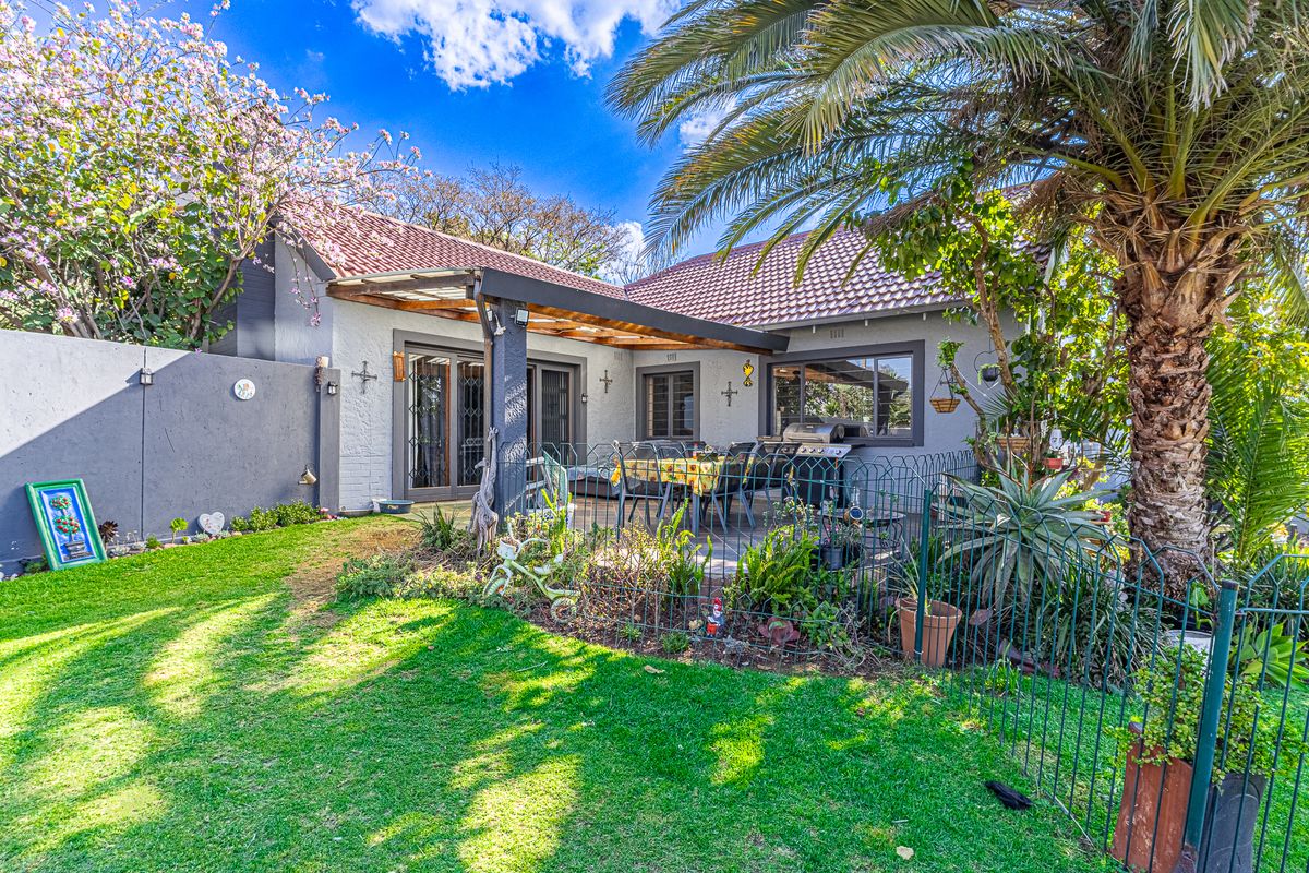 A well-maintained rear exterior view featuring a covered patio with a timber pergola, sliding glass doors, and a landscaped garden area.
