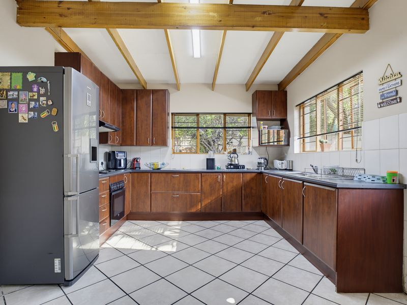 A functional U-shaped kitchen featuring dark wood cabinetry, tiled flooring, exposed timber ceiling beams, and ample natural light from multiple windows.
