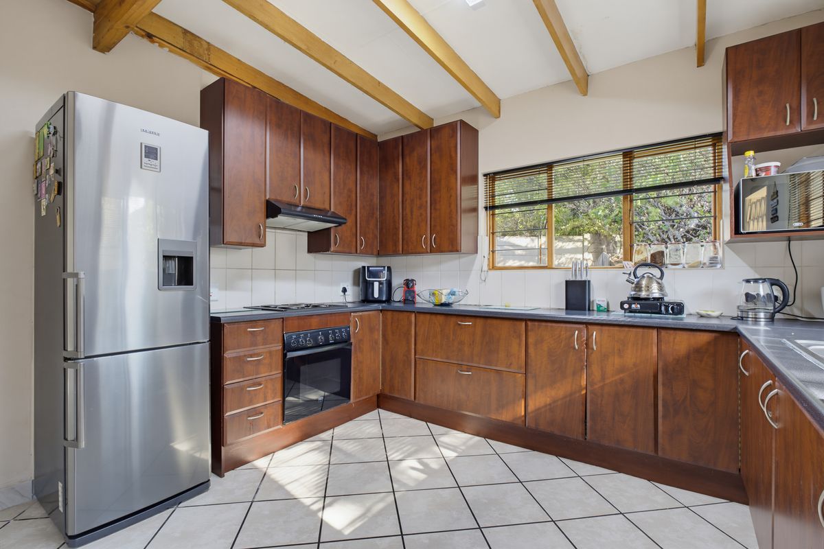 Functional kitchen featuring warm-toned wooden cabinetry, tiled flooring, exposed timber ceiling beams, and a tiled backsplash with ample counter space.