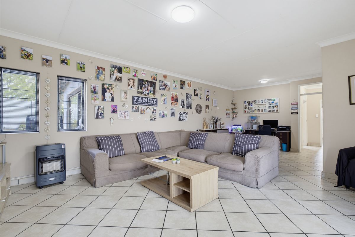 Spacious living room featuring neutral tiled flooring, coved cornicing, and ample natural light through aluminium-framed windows.