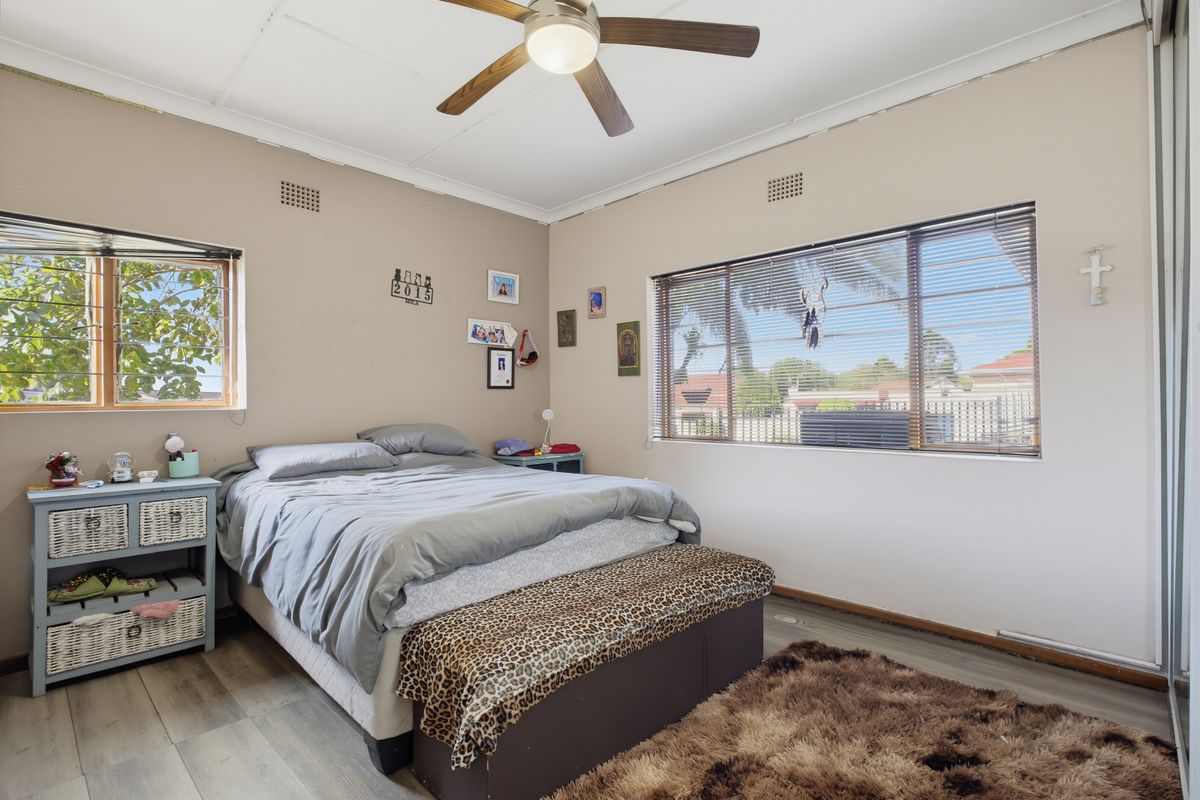 A bedroom featuring laminate flooring, a ceiling fan, and large windows with venetian blinds, offering natural light and built-in storage.