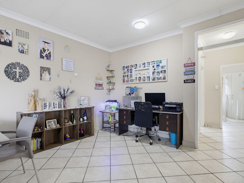 A functional living area featuring neutral tiled flooring and cove cornicing, with an open doorway leading to an adjacent bathroom.