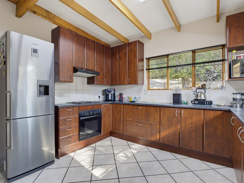 Functional kitchen featuring warm-toned wooden cabinetry, tiled flooring, exposed timber ceiling beams, and a tiled backsplash with ample counter space.
