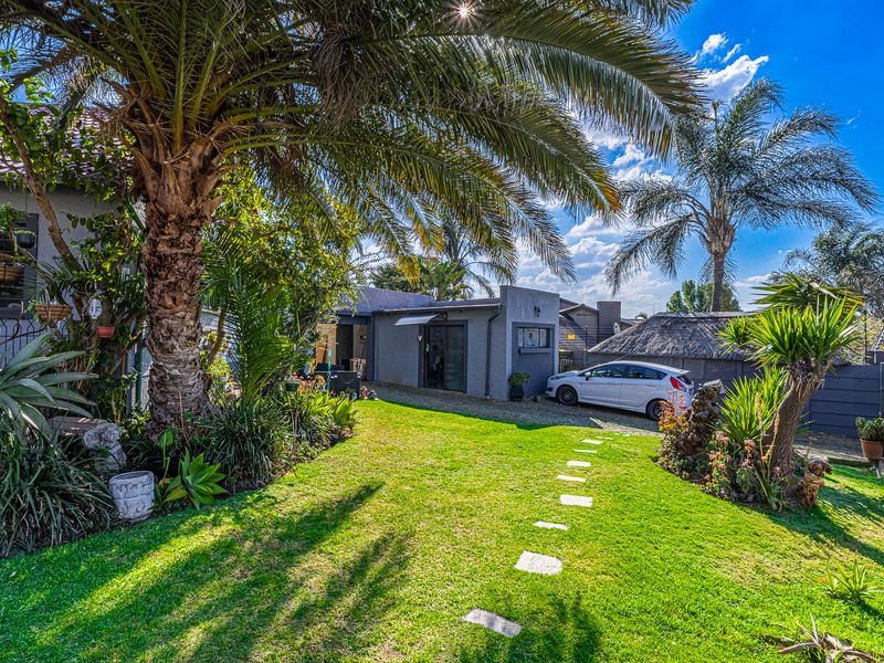 A well-maintained garden featuring a lush lawn, stone stepping stones, mature palm trees, and a paved driveway leading to the property.