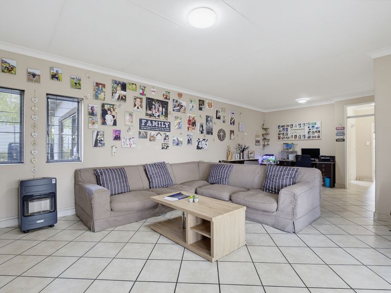 Spacious living room featuring neutral tiled flooring, coved cornicing, and ample natural light through aluminium-framed windows.