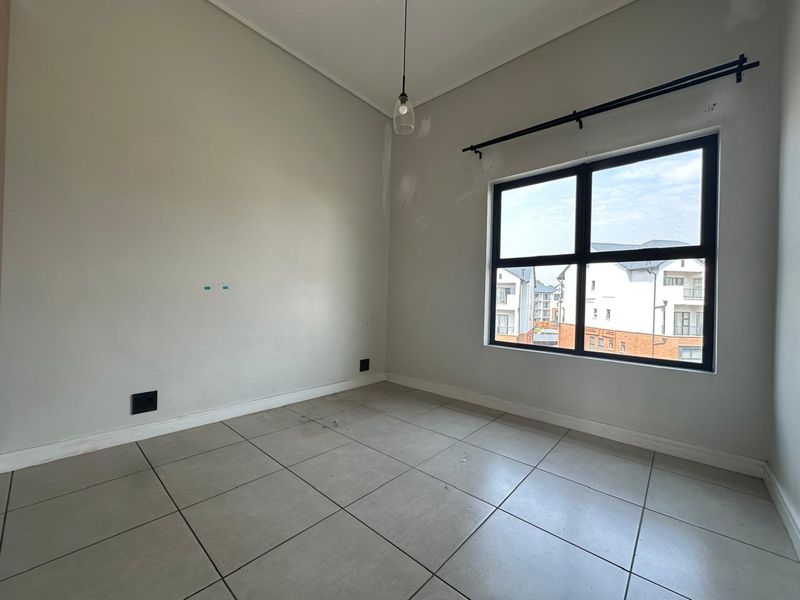 An empty bedroom featuring tiled flooring, a black-framed window, and a pendant light fixture, currently requiring minor wall repairs and cosmetic finishing.
