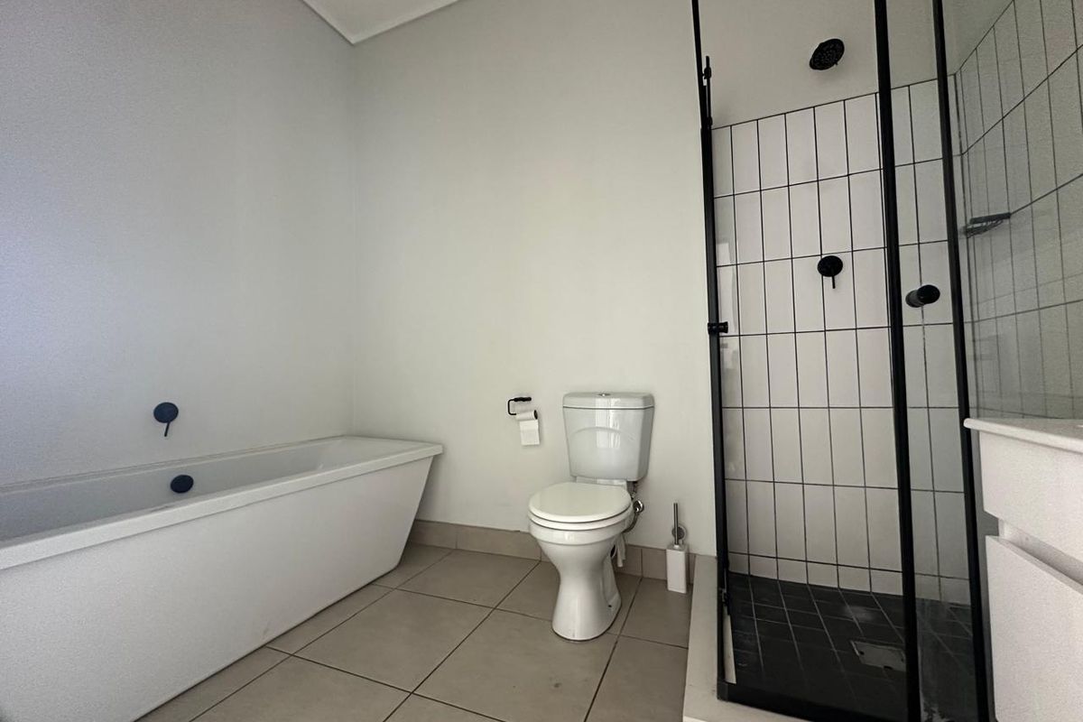 Modern bathroom featuring a freestanding bathtub, a separate shower enclosure with black fixtures, and neutral floor tiling.