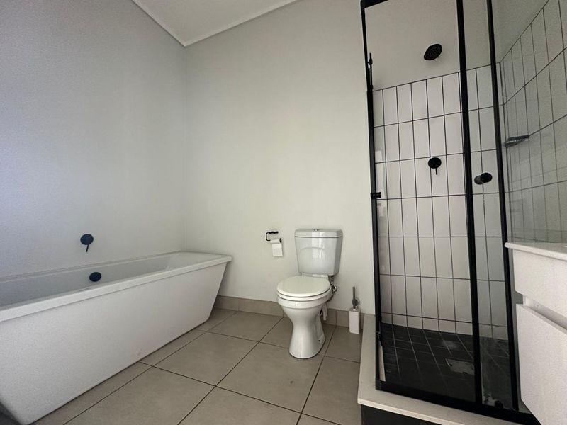 Modern bathroom featuring a freestanding bathtub, a separate shower enclosure with black fixtures, and neutral floor tiling.