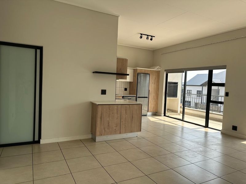 Spacious open-plan living area featuring tiled floors, modern wood-finish kitchen cabinetry, and large sliding doors leading to a balcony.
