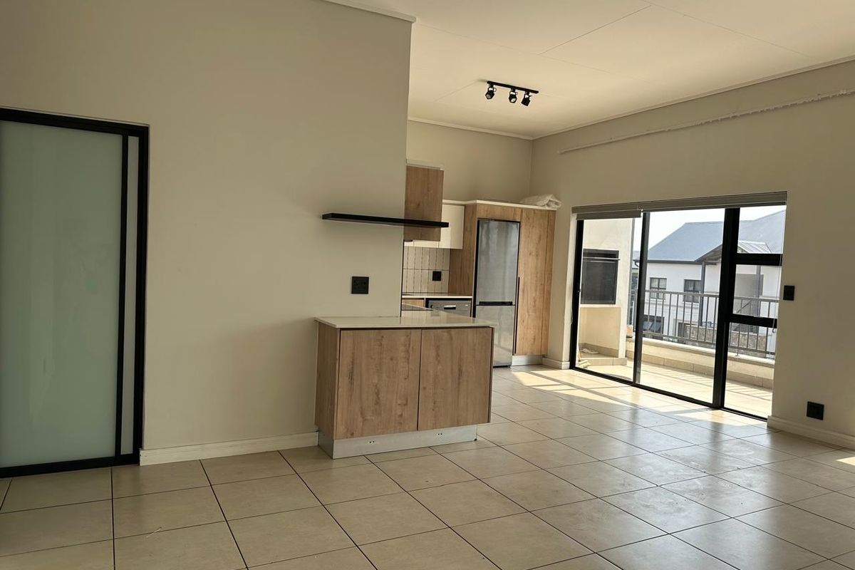 Spacious open-plan living area featuring tiled floors, modern wood-finish kitchen cabinetry, and large sliding doors leading to a balcony.