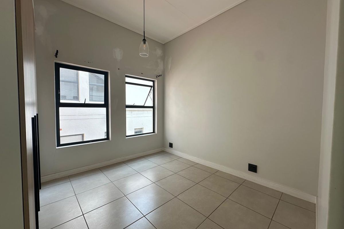 An empty bedroom featuring tiled flooring, built-in cupboards, and modern aluminium windows, currently requiring minor wall finishing and paint touch-ups.