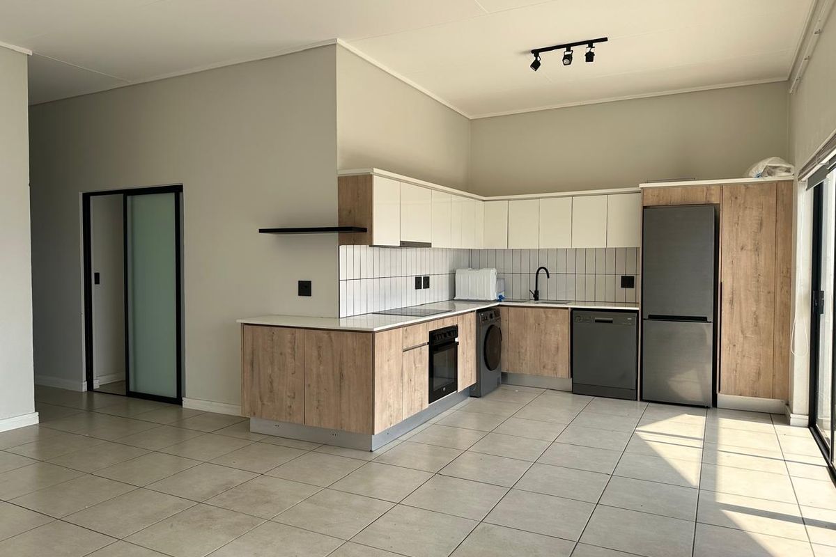 Modern open-plan kitchen featuring light wood-grain and white cabinetry, tiled backsplash, integrated oven, hob, and sleek black fixtures in a spacious tiled area.