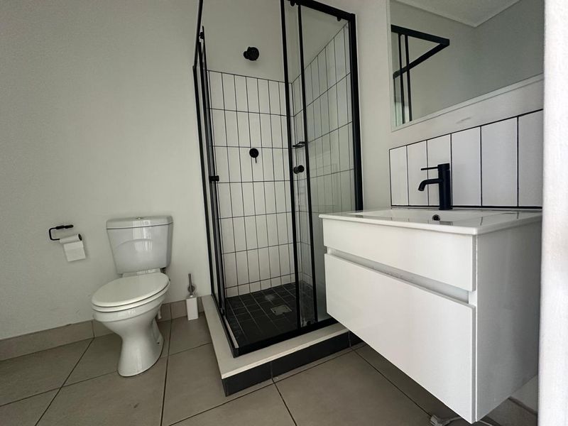 Modern bathroom featuring a walk-in shower with black frame, contemporary vanity with basin, and clean tiled finishes.