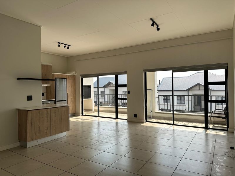 Spacious open-plan living area featuring tiled floors, modern kitchen cabinetry, and large sliding doors leading to a private balcony.