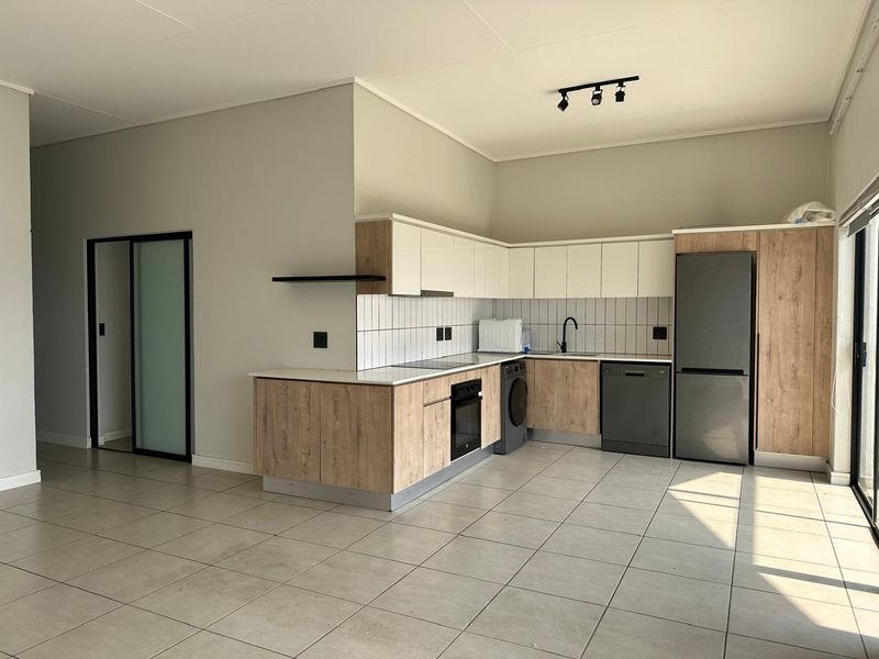 Modern open-plan kitchen featuring light wood-grain and white cabinetry, tiled backsplash, integrated oven, hob, and sleek black fixtures in a spacious tiled area.