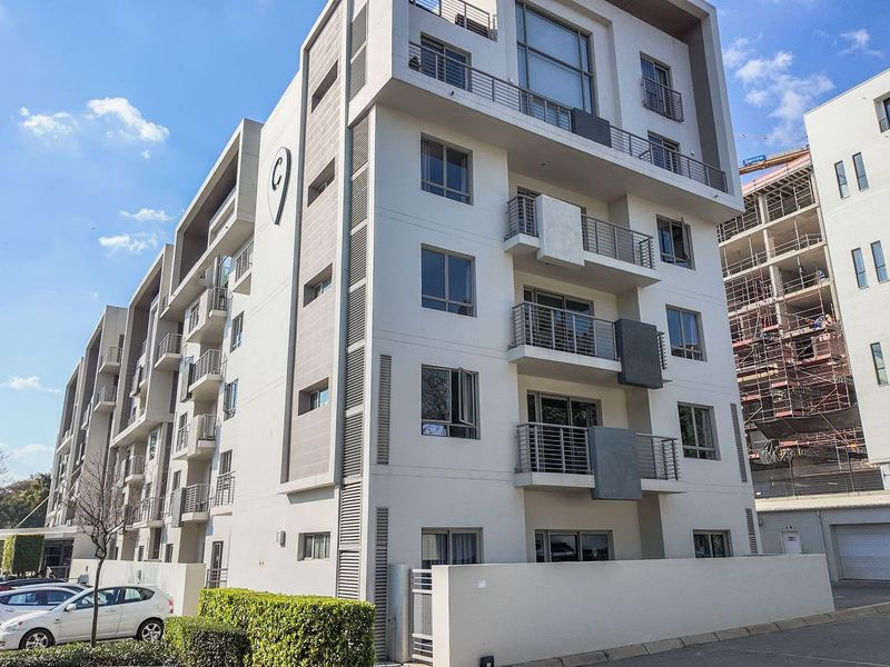 Modern multi-story apartment building featuring contemporary architectural design, private balconies with metal railings, and a paved driveway entrance.
