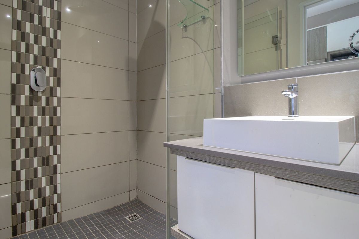 Modern bathroom featuring a glass-enclosed shower with mosaic tile accents, a sleek vanity cabinet with a countertop basin, and a wall-mounted mirror.
