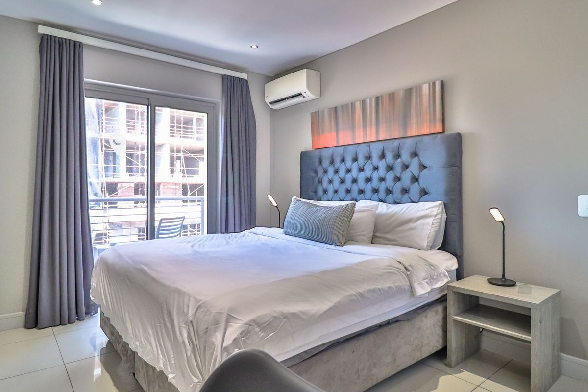 A well-maintained bedroom featuring tiled flooring, recessed lighting, an integrated air conditioning unit, and a sliding glass door leading to a balcony.