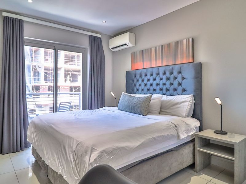 A well-maintained bedroom featuring tiled flooring, recessed lighting, an integrated air conditioning unit, and a sliding glass door leading to a balcony.