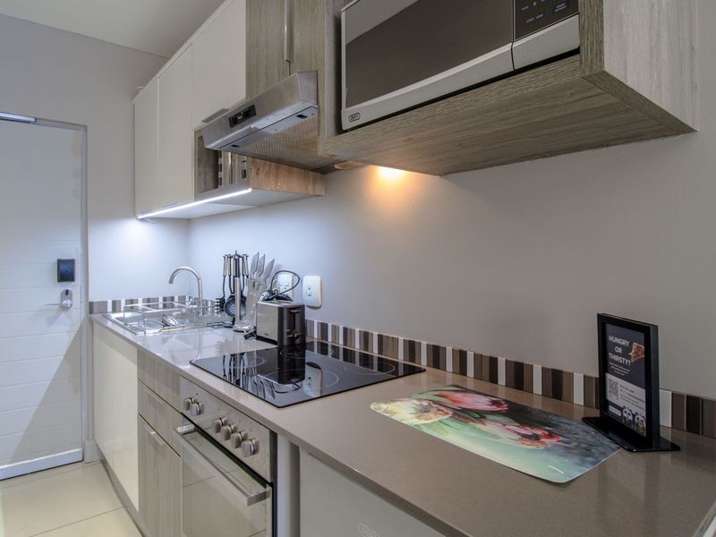 Modern kitchen featuring sleek cabinetry, stone countertops, integrated electric hob, oven, extractor fan, and built-in microwave with a tiled backsplash.