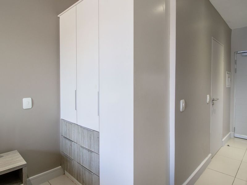 A clean, modern bedroom featuring neutral wall tones, tiled flooring, and a functional built-in wardrobe with integrated storage.