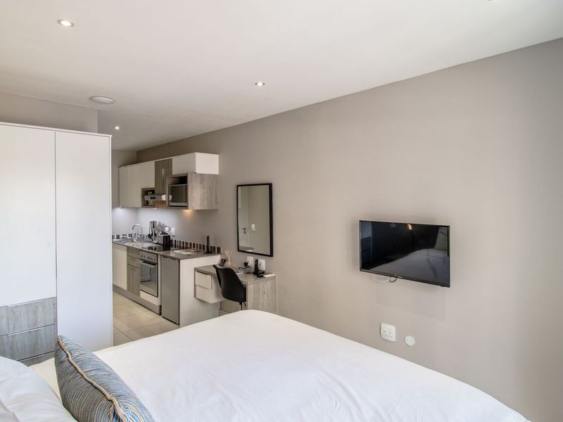 A modern open-plan studio apartment featuring a compact kitchenette with built-in cabinetry, integrated appliances, and a functional bedroom area with ample storage.