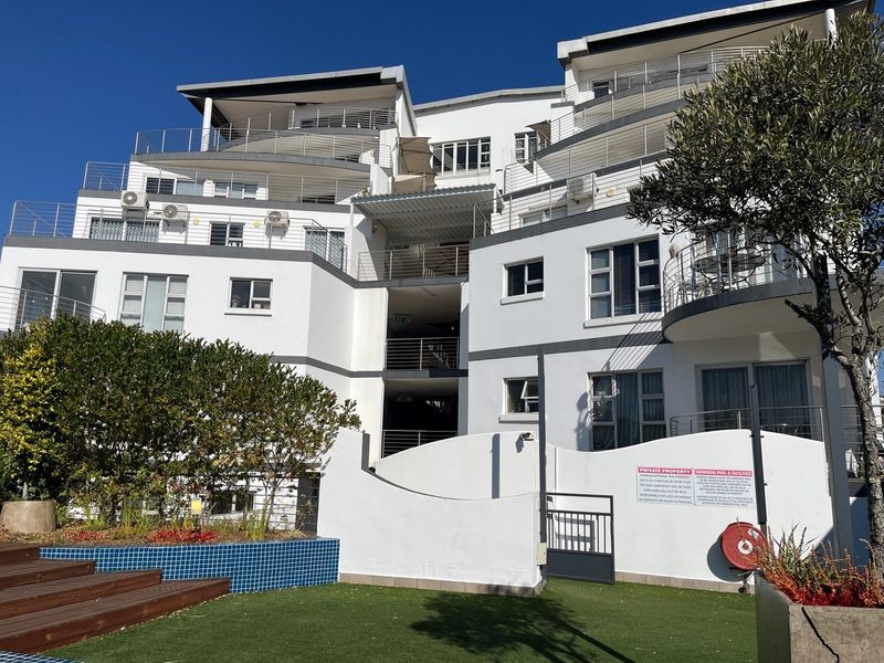 Rear view of a modern apartment complex featuring multi-level balconies, a swimming pool area with decking, and well-maintained exterior finishes.
