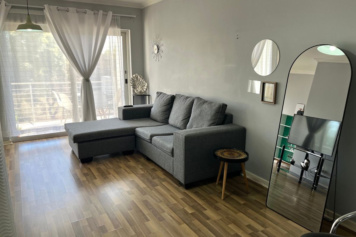 A well-maintained living room featuring laminate flooring, neutral wall tones, and a sliding glass door providing access to an outdoor balcony area.