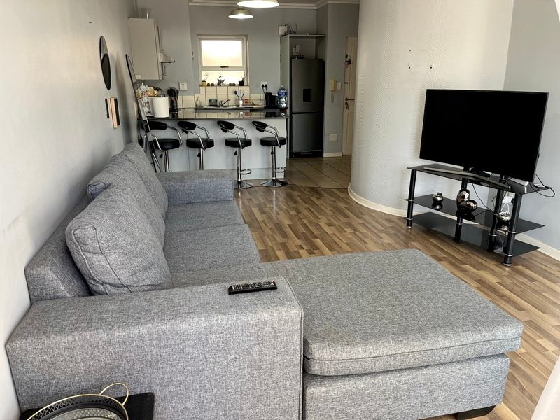 Open-plan living area featuring laminate flooring, a curved feature wall, and a functional kitchen with a breakfast bar and tiled splashback.