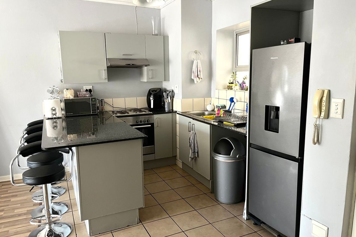 Functional kitchen featuring granite countertops, built-in oven, hob, extractor fan, and ample cabinetry with tiled flooring.