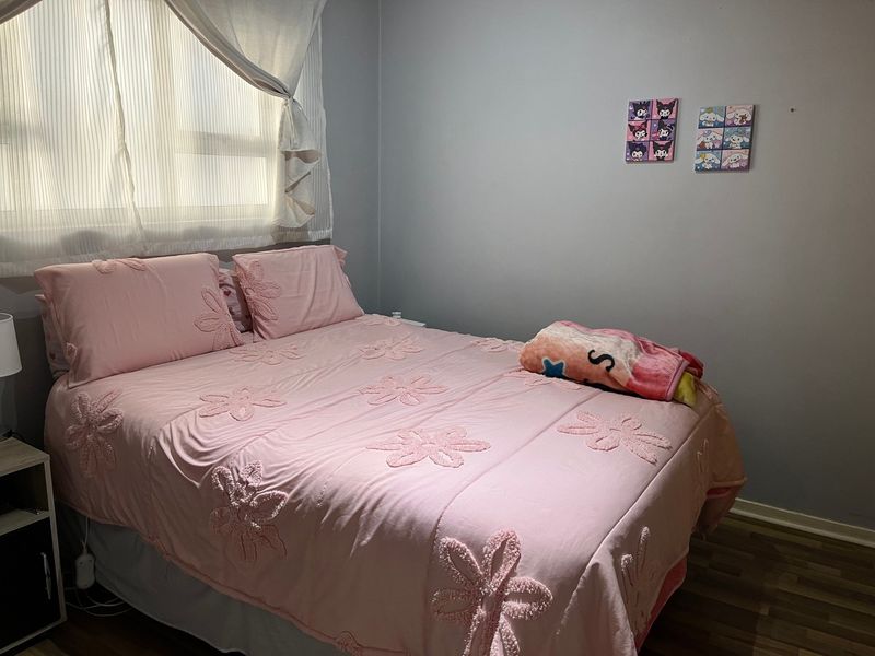 A standard bedroom featuring laminate flooring and window blinds, providing a functional space for rest.