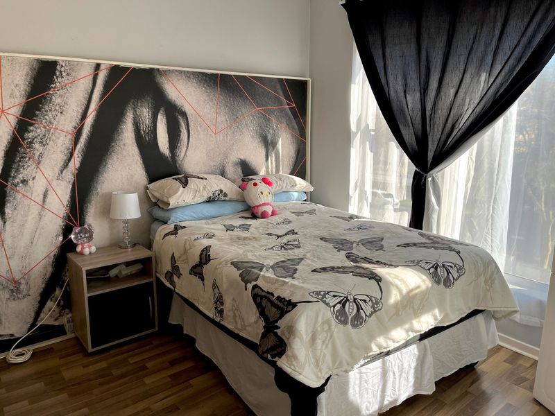 A bedroom featuring laminate flooring and a large window, providing natural light to the space.