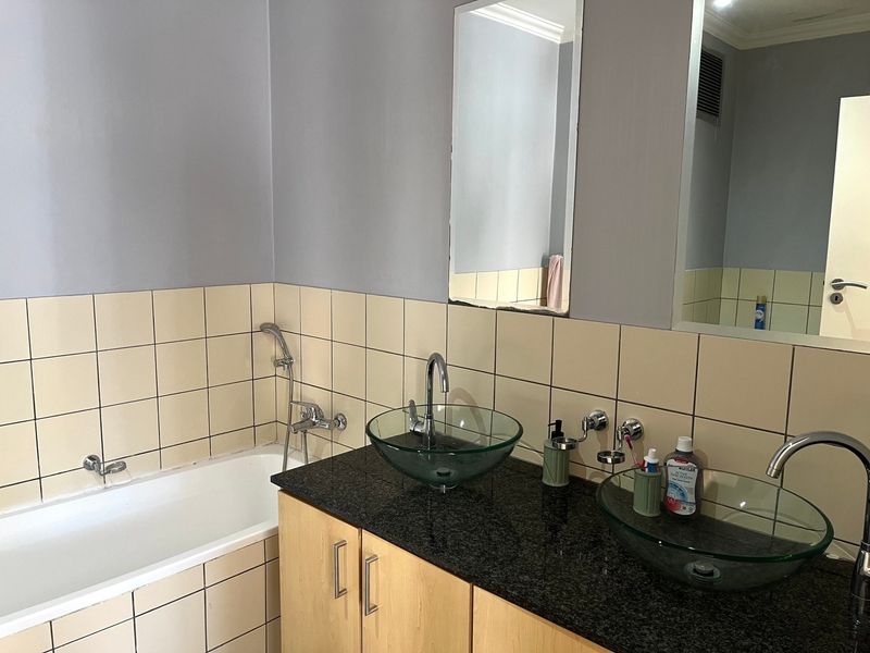 Bathroom featuring a dual vanity with glass vessel sinks, granite countertop, wooden cabinetry, and a bathtub with tiled surround.