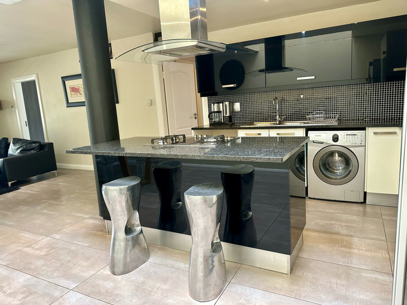 Modern open-plan kitchen featuring a granite island with gas cooktop, sleek black cabinetry, mosaic backsplash, and integrated laundry appliances.