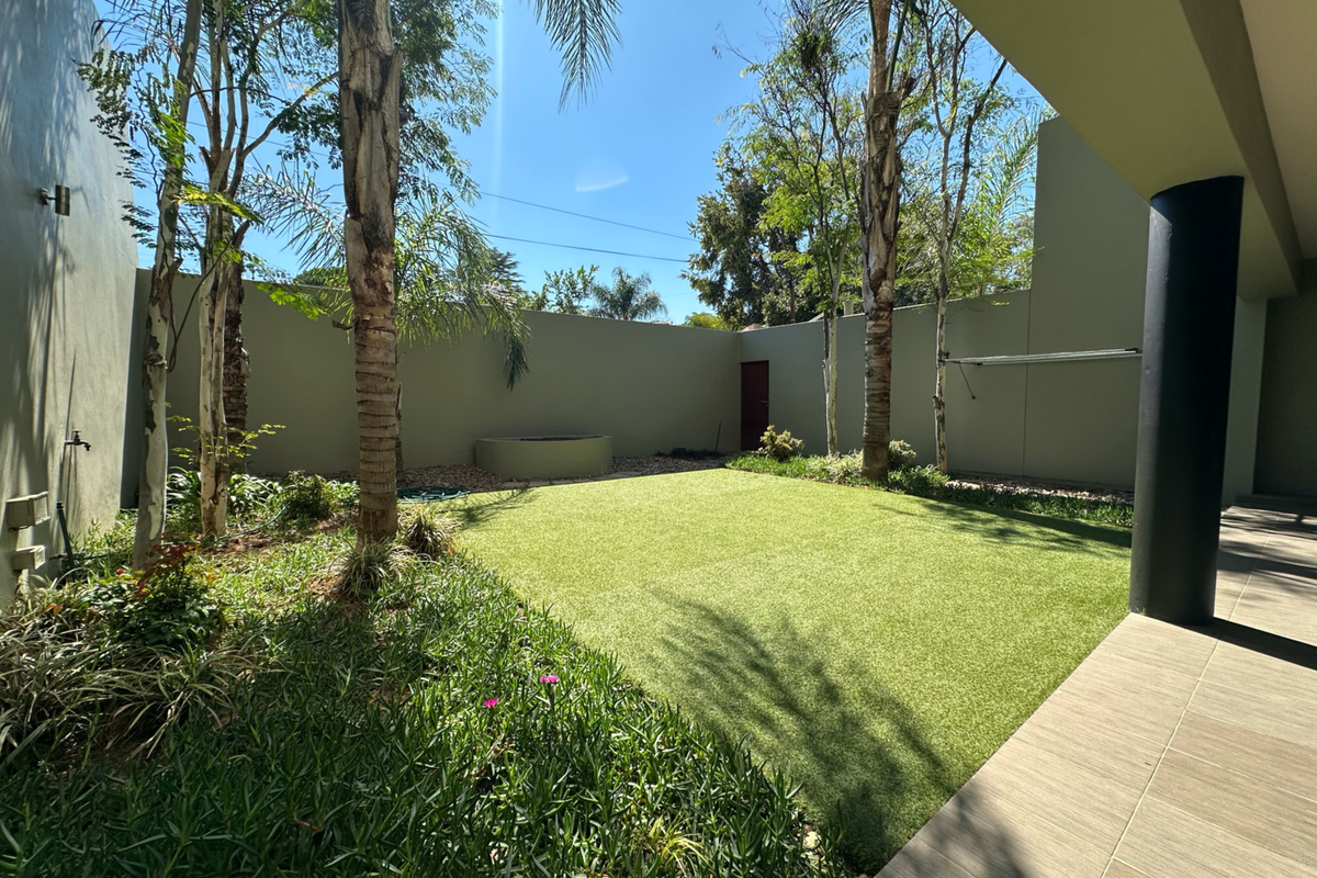A private rear garden featuring a well-maintained artificial lawn, perimeter boundary walls, and a covered tiled patio area.